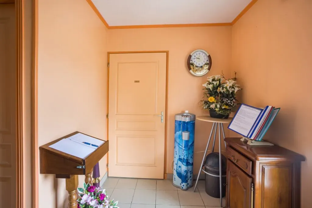Espace d'accueil intérieur avec registre de condoléances, meuble en bois et fontaine à eau.