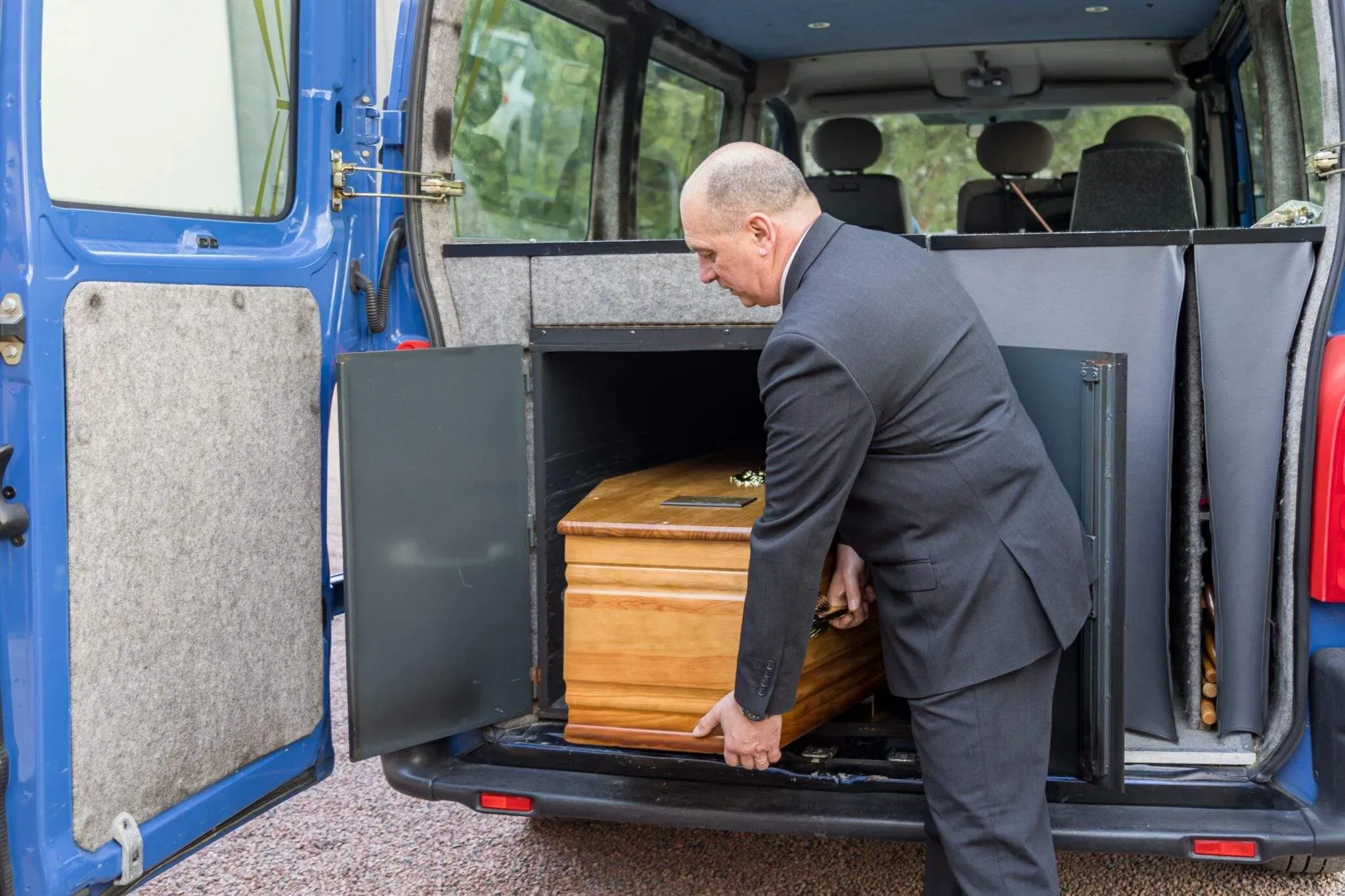 Agent funéraire insérant un cercueil en bois dans l'arrière du fourgon.